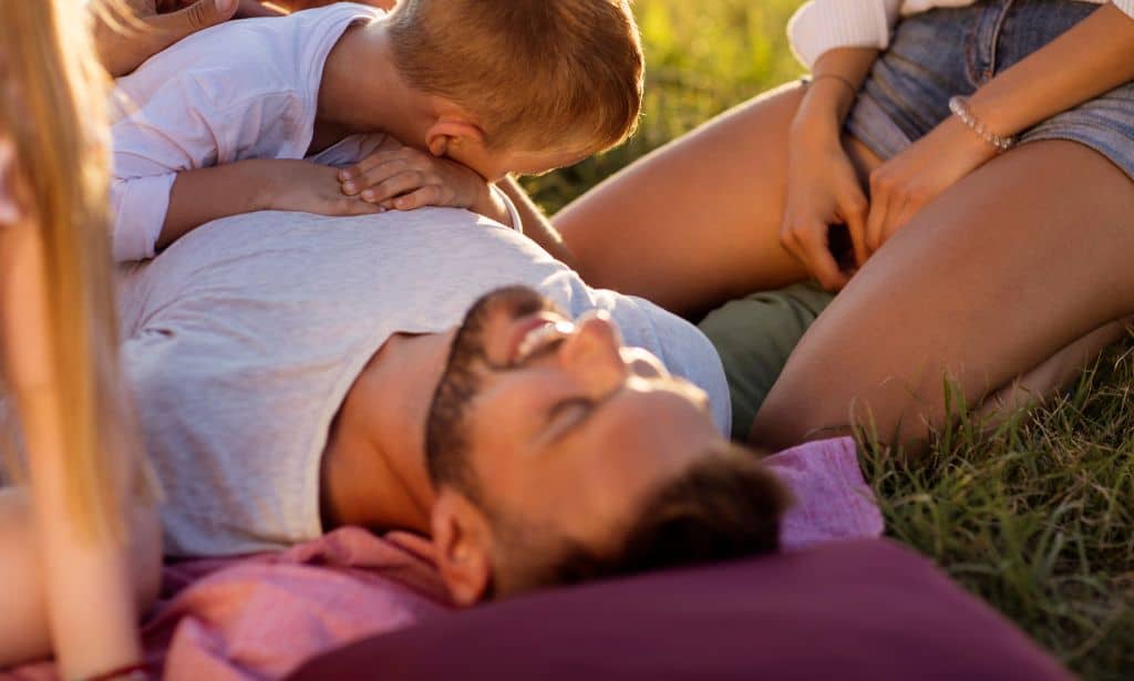 A baby sleeping on a man while a woman watches them with a smile