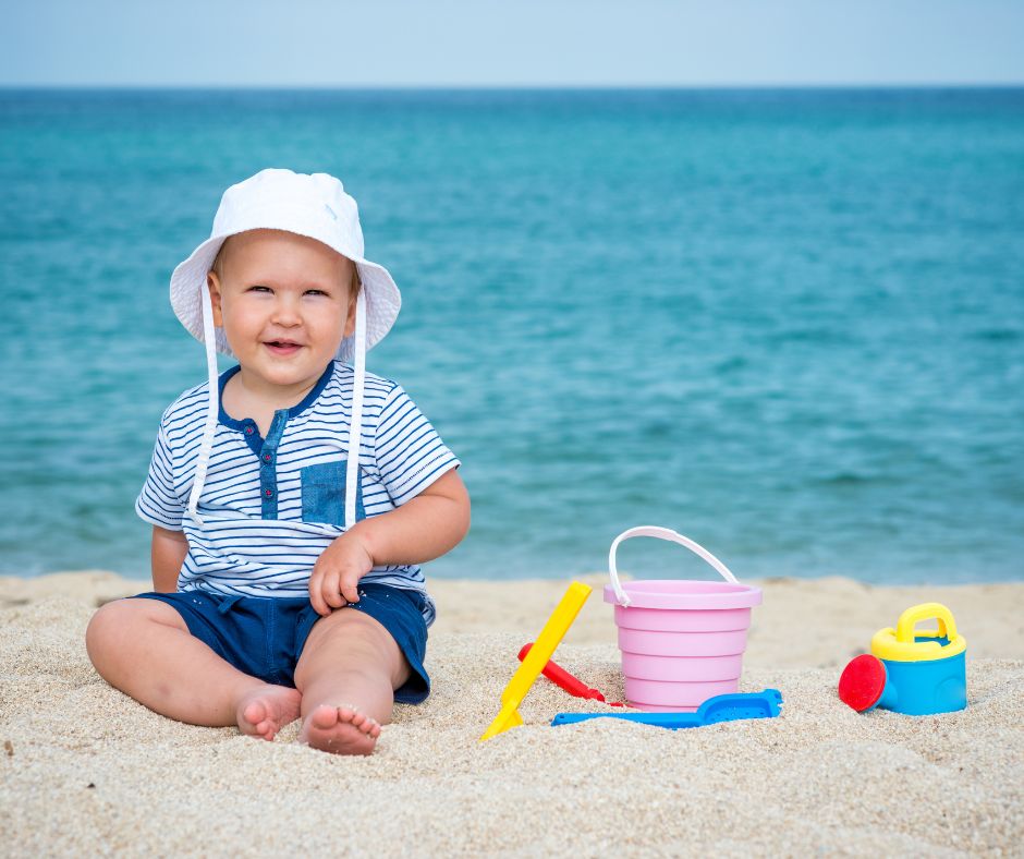 Toddler seated on the beach wearing a hat