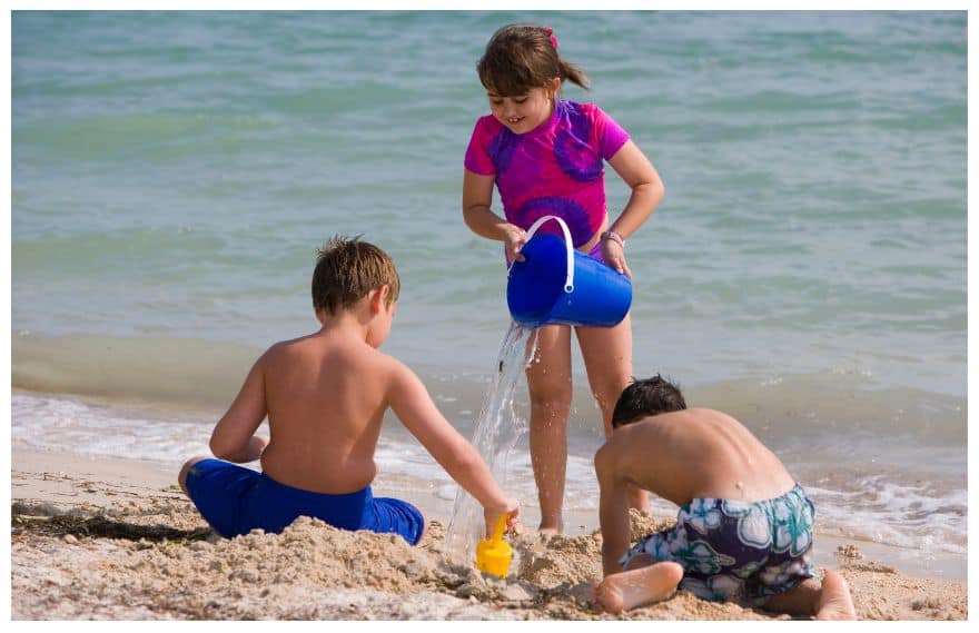 A girl pouring water at the beach playing with siblings
