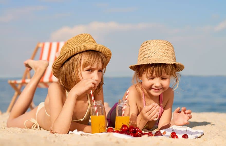 Two girls drinking juice and eating berries at the beach