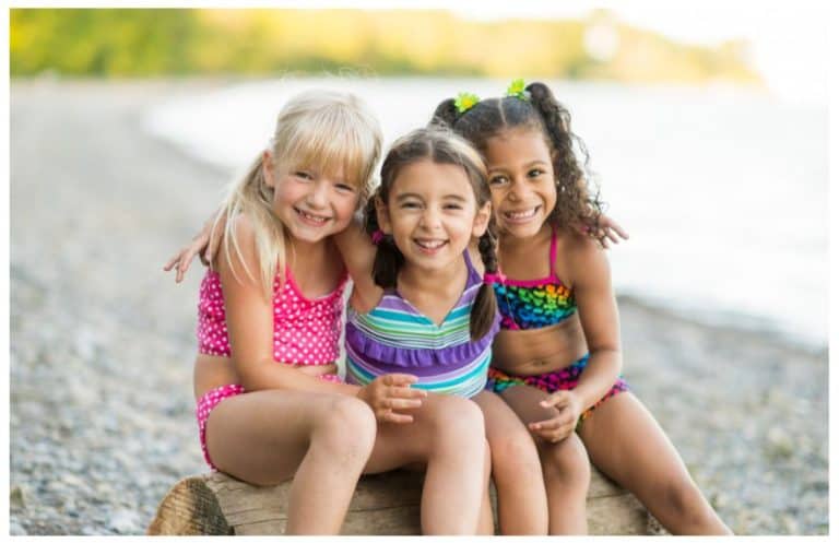 Three girls sited on a log at the beach smiling