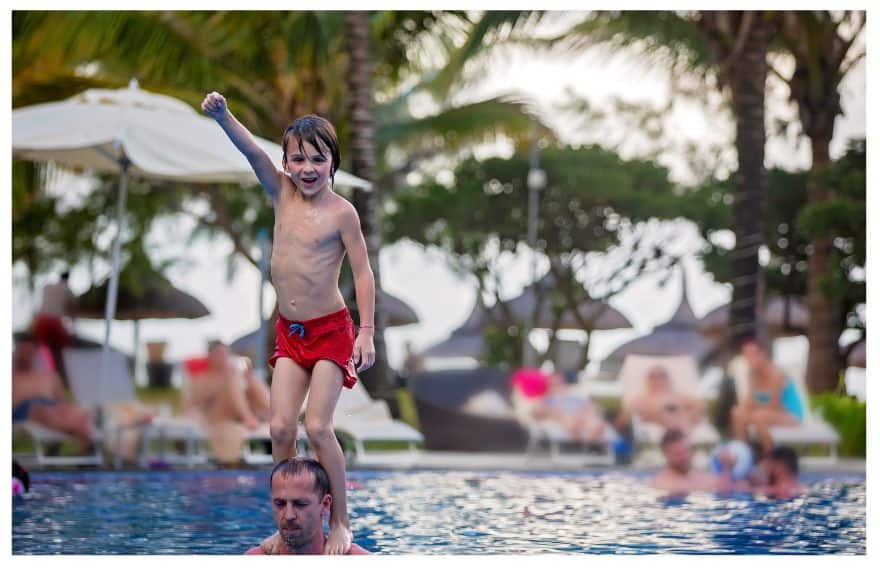 A boy standing on a man's shoulders at the pool