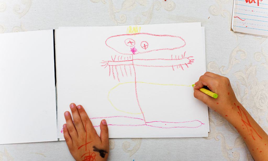 A kid drawing using a yellow crayon