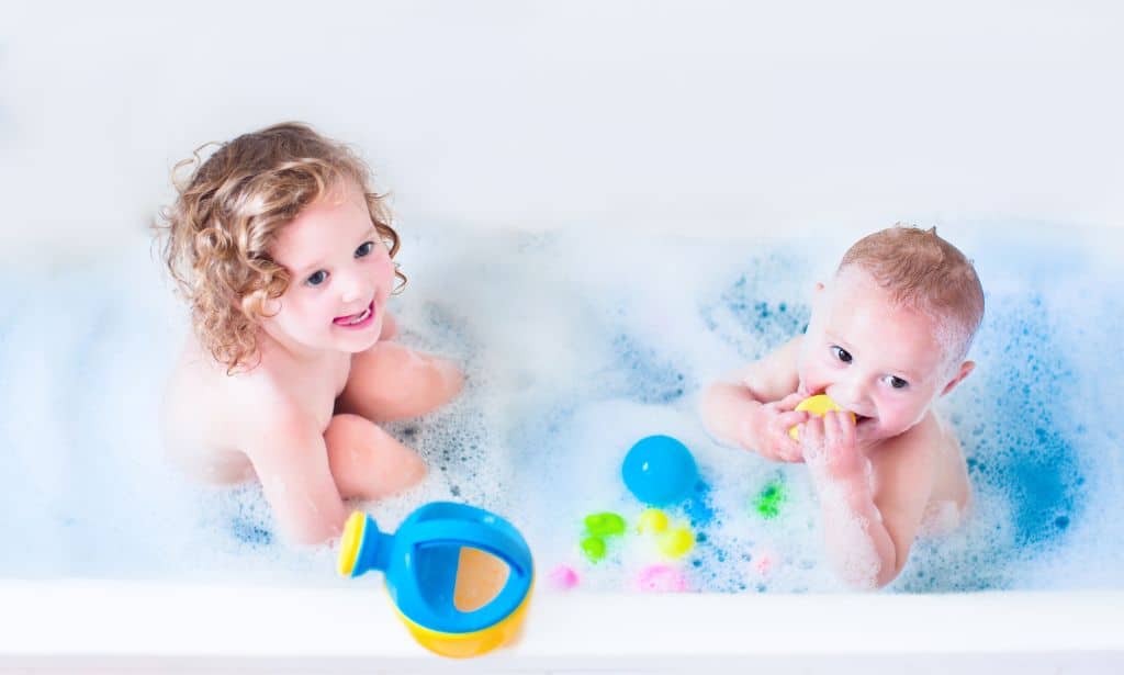 A toddler and baby having a bath with bubbles and bath toys